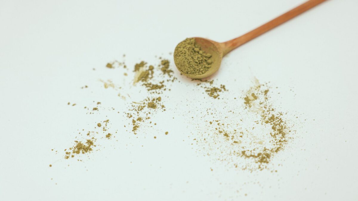 Flat lay image of organic matcha powder with wooden spoon on a clean white background.