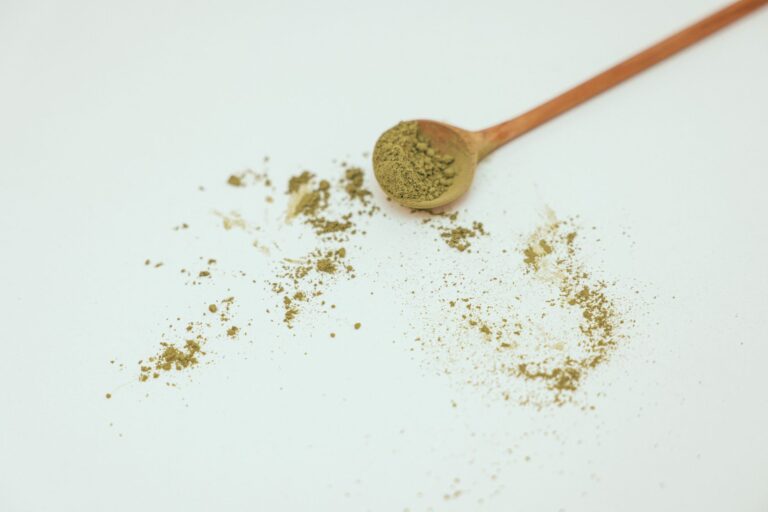 Flat lay image of organic matcha powder with wooden spoon on a clean white background.