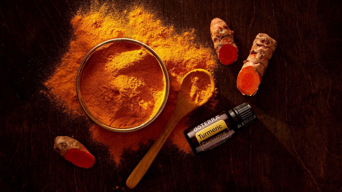 Top view of turmeric powder, curcuma roots, and essential oil on wooden surface.