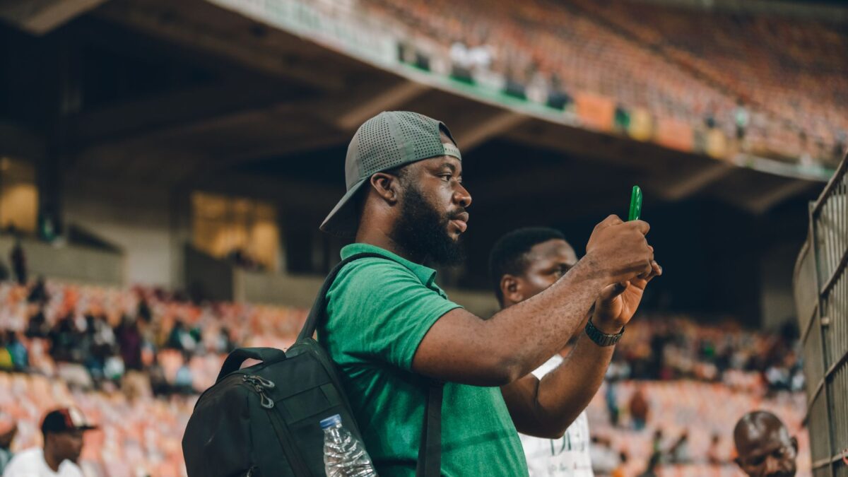 Smartphone mit Sport-App vor einem Stadion im Hintergrund