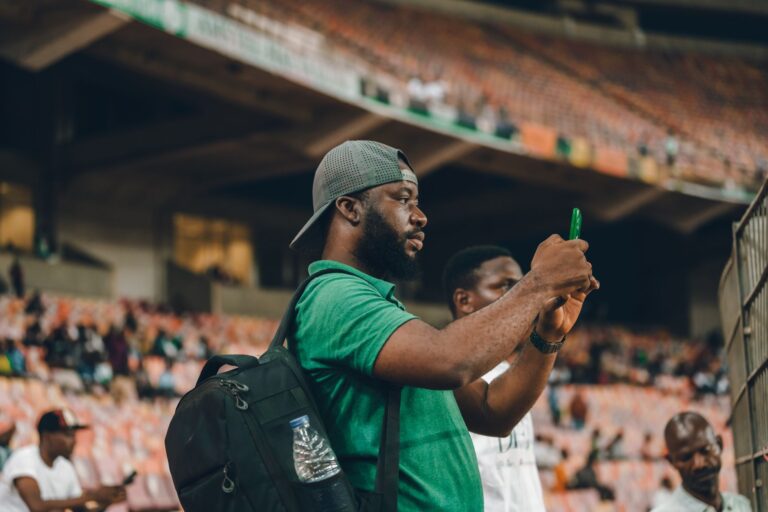 Smartphone mit Sport-App vor einem Stadion im Hintergrund