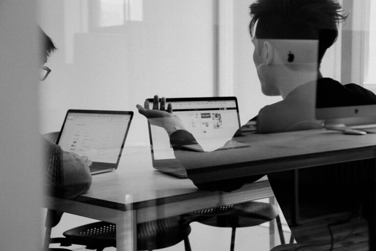 Zwei Personen analysieren Kursdaten und Handelsplattformen am Laptop im Büro